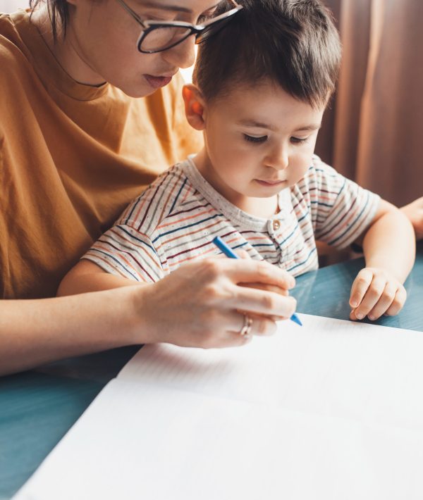 Close up photo of a caucasian mother helping her son to write at home Close up photo of a caucasian mother helping her son to write at home